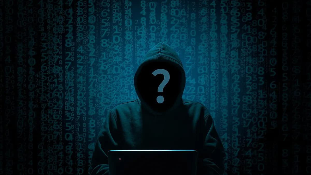 Hooded figure at a laptop against a wall of code