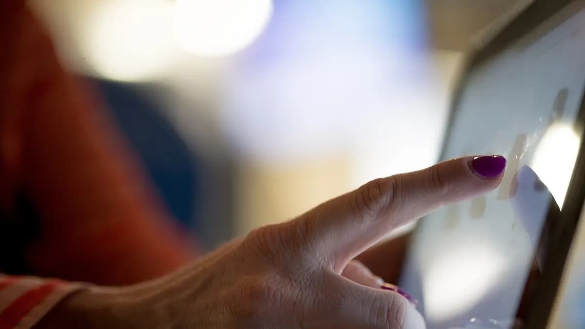 A fingertip pressing the screen of a tablet, seen close up from the side