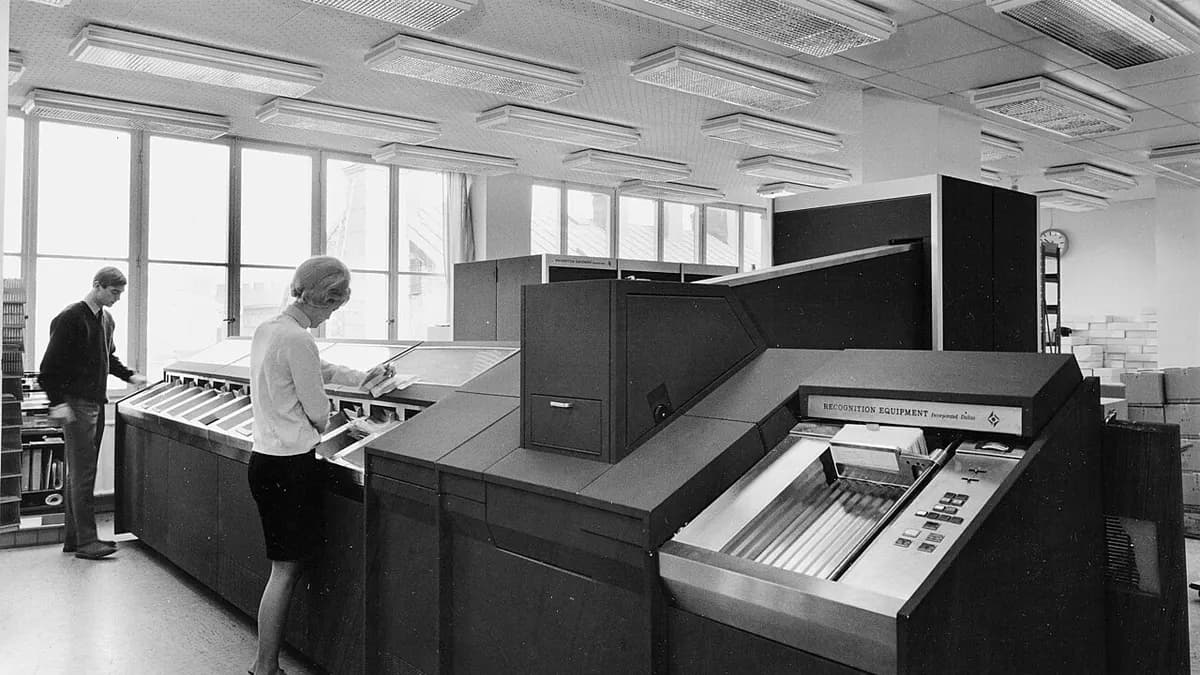 A 1960s mainframe computer room with operators at the consoles